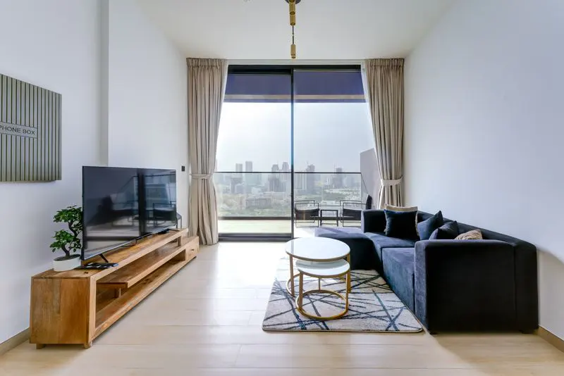 Bright living room with a dark blue sectional sofa, a wooden TV stand, and a city view through large windows.