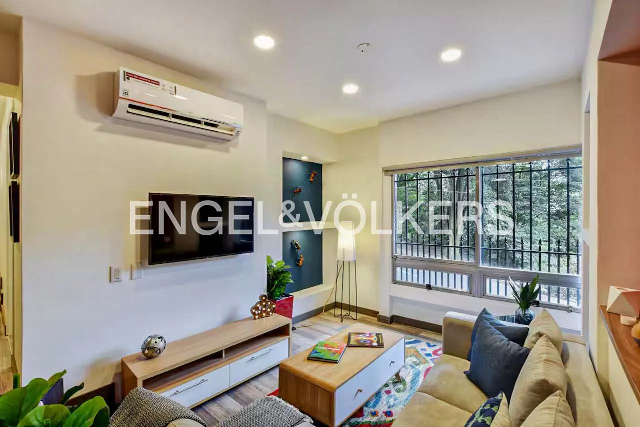 Bright living room with a beige sofa, wood coffee table, TV, and large window with a view of trees.