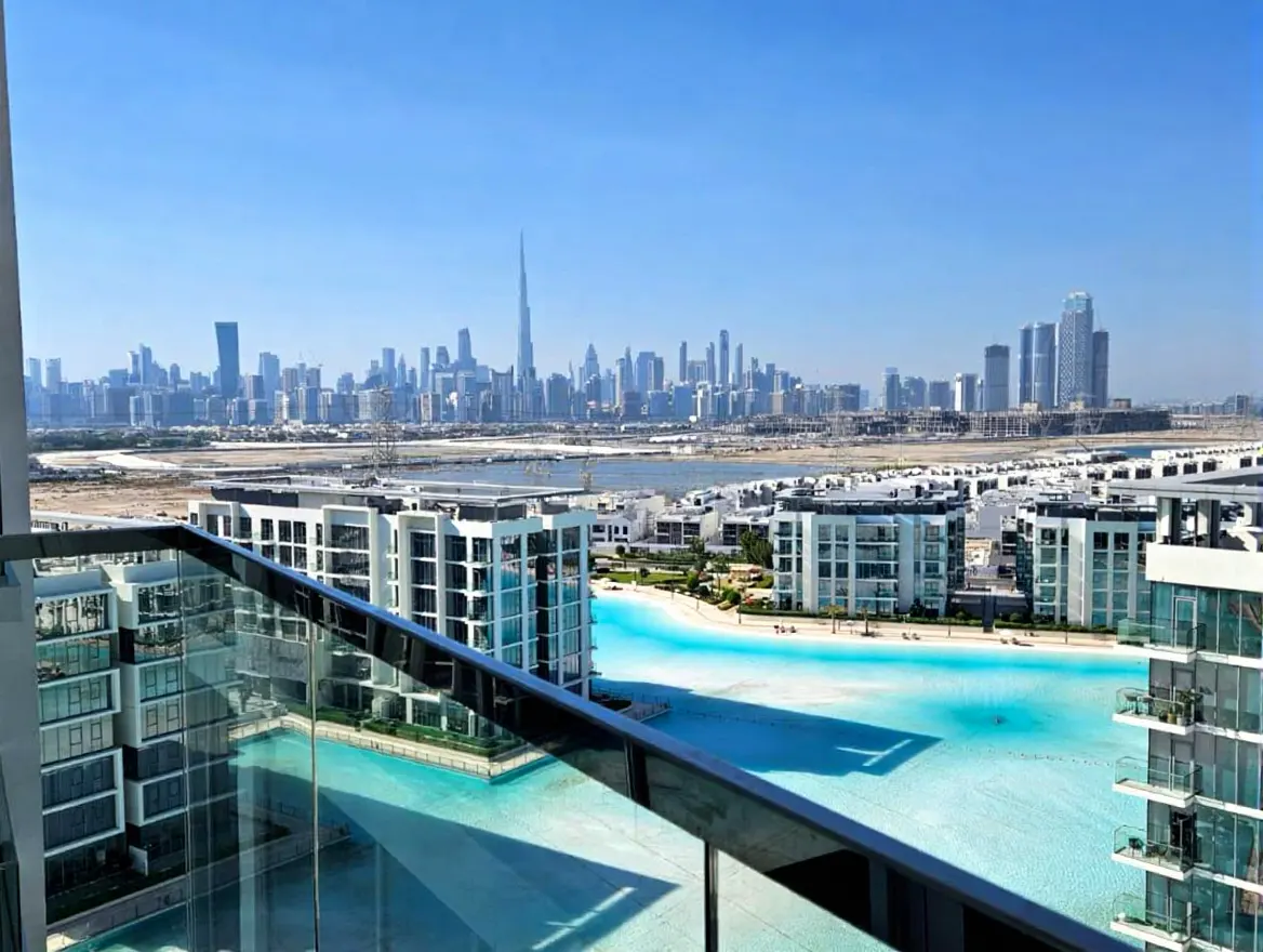 View from a balcony overlooking a turquoise lagoon and white buildings, with the Dubai skyline and Burj Khalifa in the background.