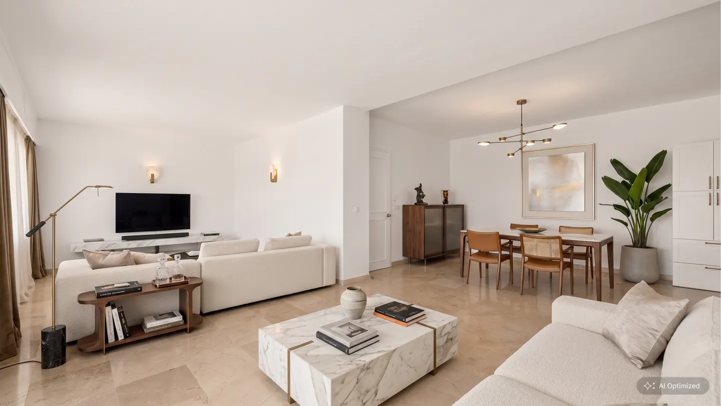 Bright, open-concept living and dining area with white walls, marble coffee table, and tan leather dining chairs.
