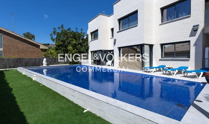 A modern white house with a blue tiled pool and blue lounge chairs on a sunny day.