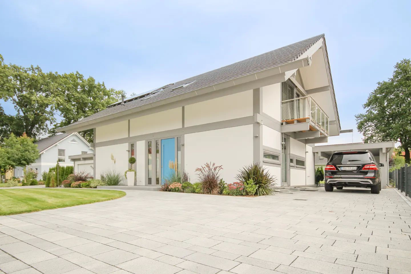 Modern white house with gray trim, a bright blue front door, a balcony, and a black car parked in the driveway.