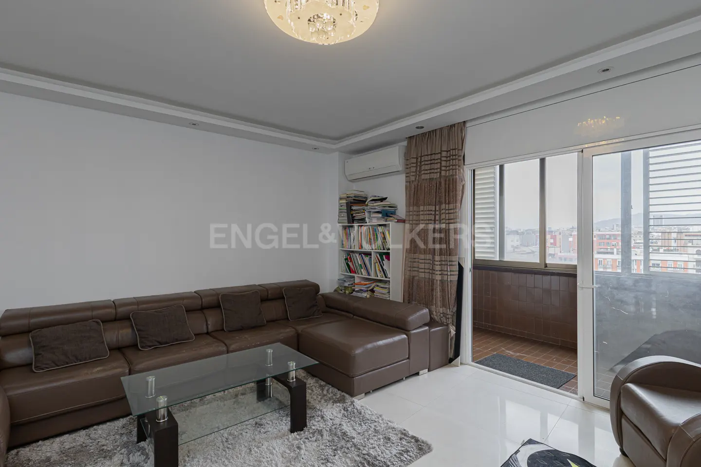 Living room with brown leather sectional sofa, glass coffee table on gray rug, and balcony with city view.