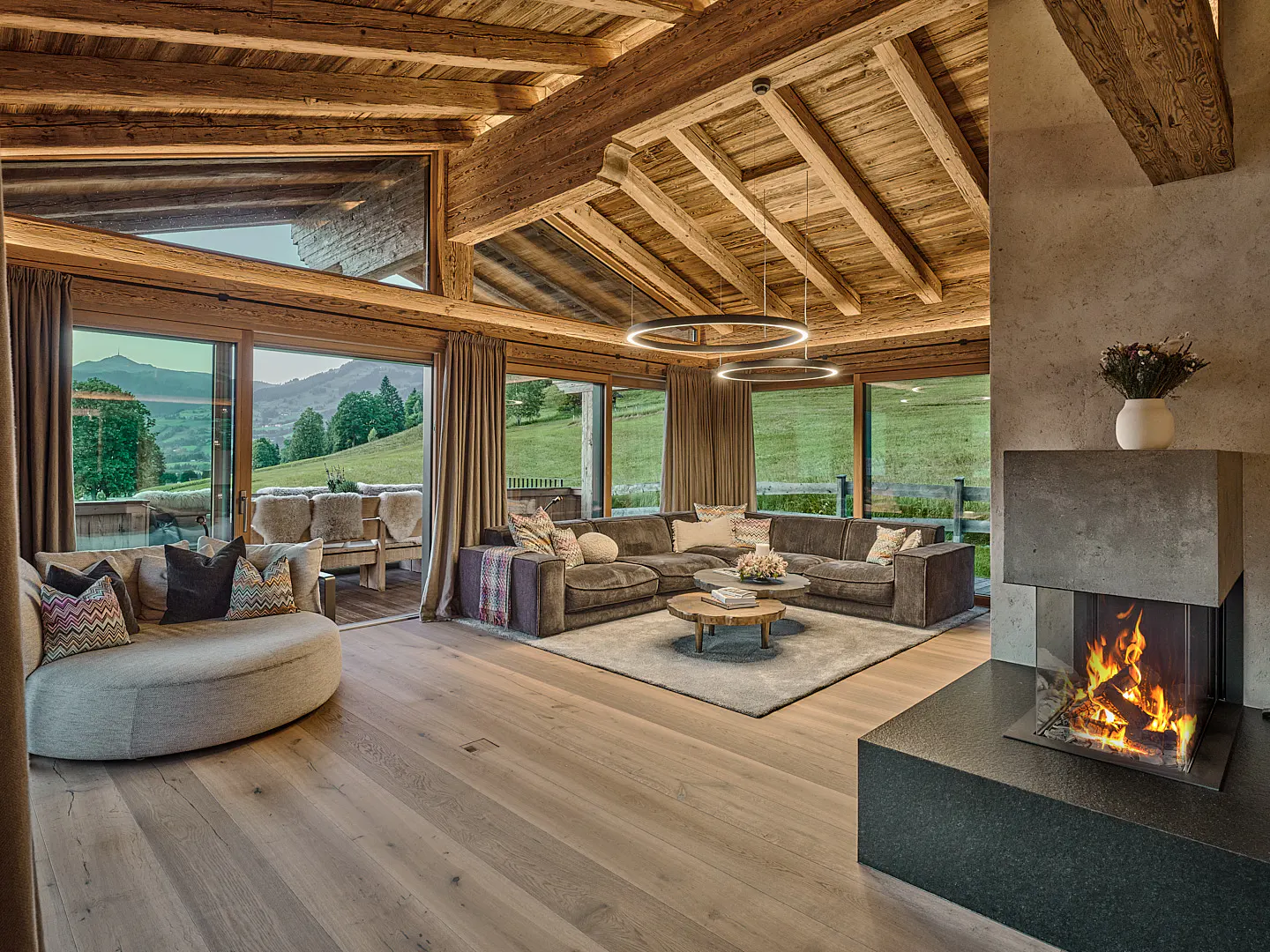 Modern mountain living room with wood-beamed ceiling, large windows, sectional sofa, and a contemporary glass fireplace.