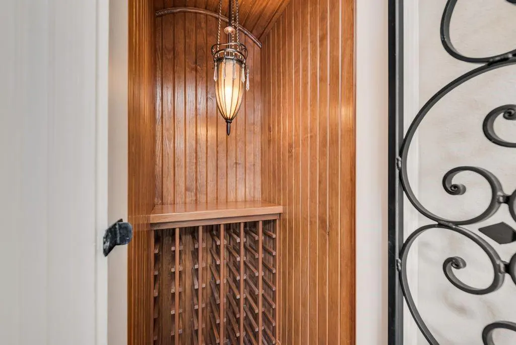 Built-in wooden wine rack with a hanging light fixture. The walls are wood paneling. A decorative iron gate is partially visible.