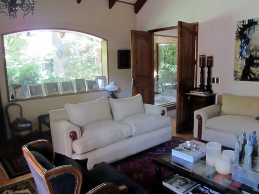 Living room with white sofas, dark wood doors, and a large arched window overlooking greenery. A glass coffee table sits on a patterned rug.