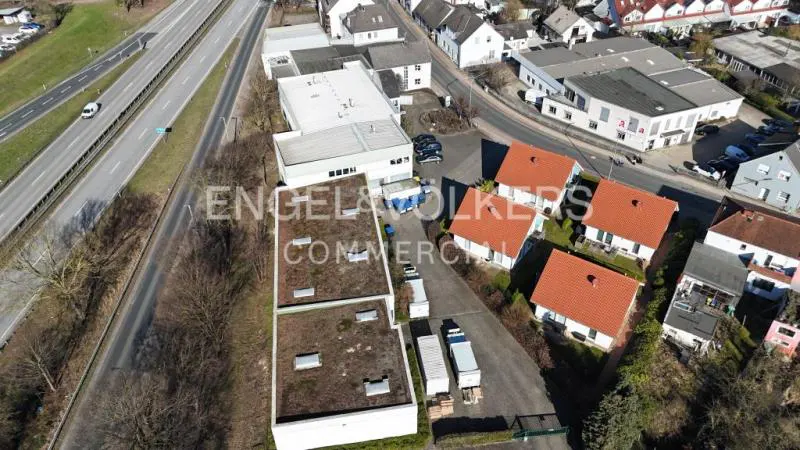 Aerial view of commercial buildings with flat roofs, trucks, and houses with red roofs, near a highway.
