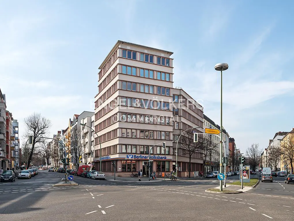 A multi-story beige commercial building with a Berliner Volksbank branch on the ground floor at a sunny city intersection.