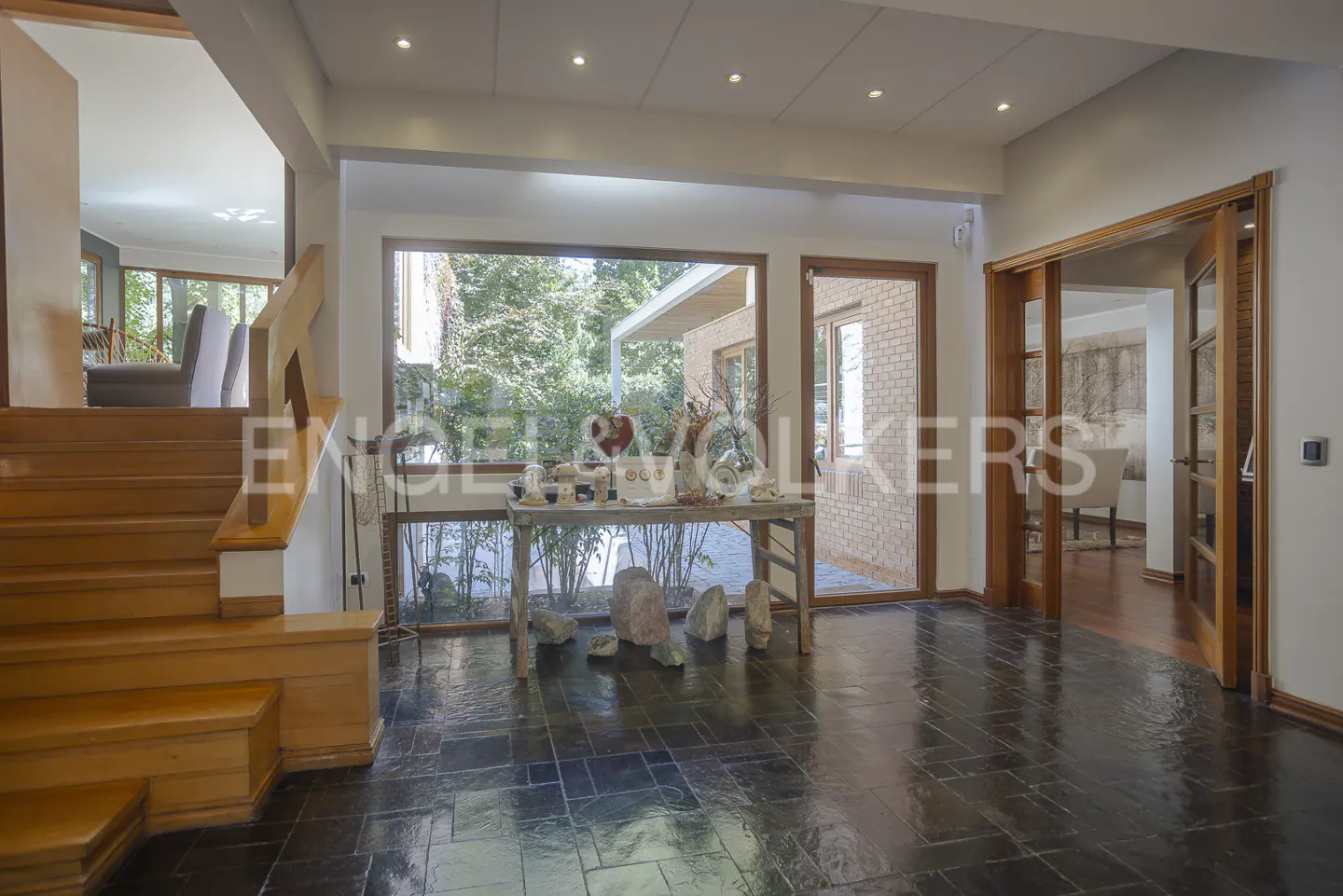 A home's entryway with wood stairs, a table with decor, and a view of the outdoors. The floor is dark tile.