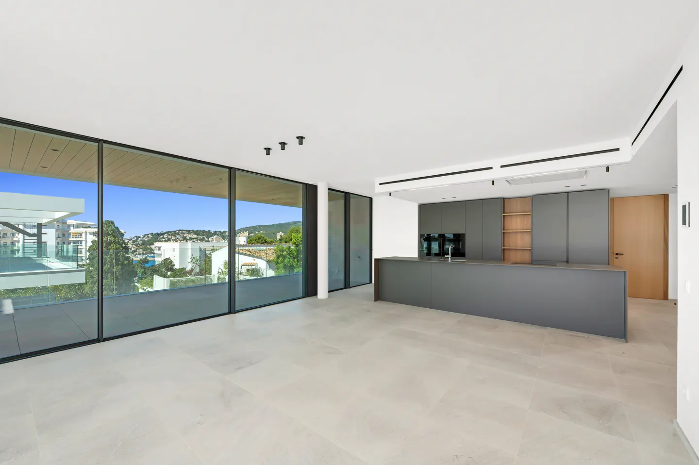 Bright, modern open-concept kitchen and living space with gray cabinets and large windows overlooking a coastal view.
