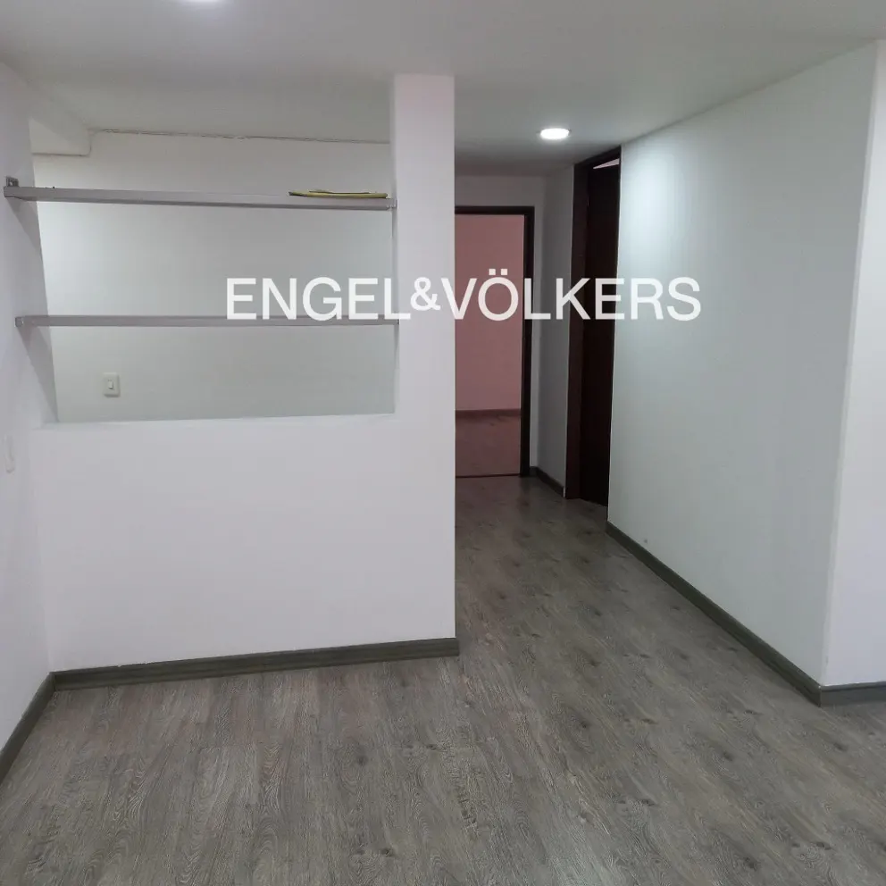 Empty room with gray wood floors, white walls, and Engel & Völkers logo. A doorway leads to another room.