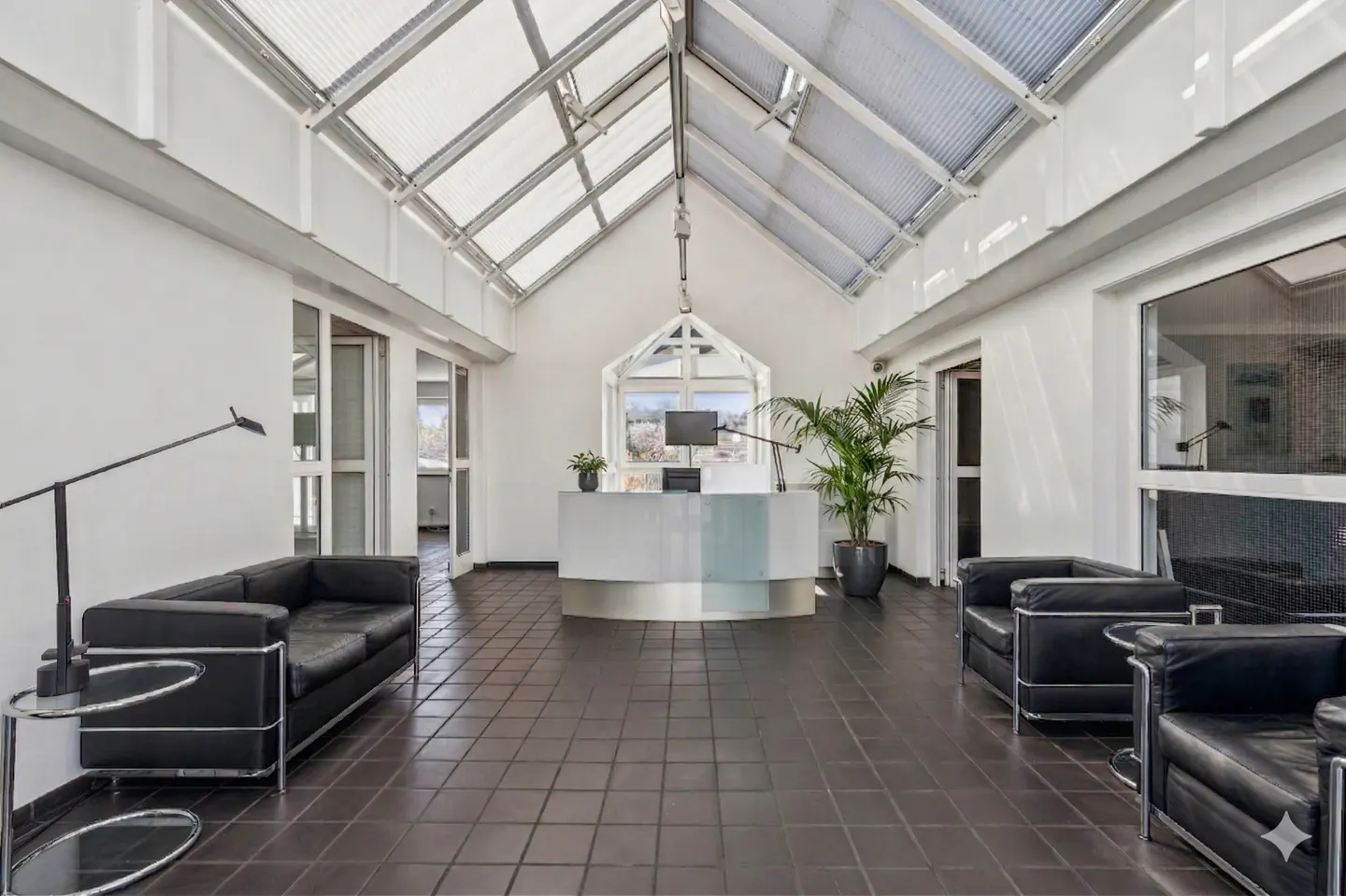 Bright, modern office lobby with a white reception desk, black leather seating, and a skylight roof.