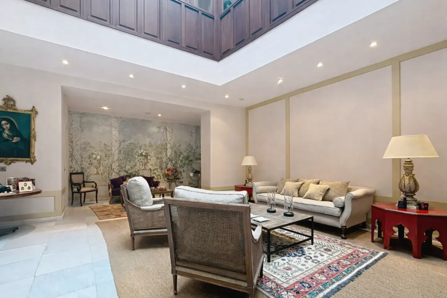 Bright living room with beige walls, a floral mural, and a skylight. A sofa, chairs, and a patterned rug create a cozy seating area.