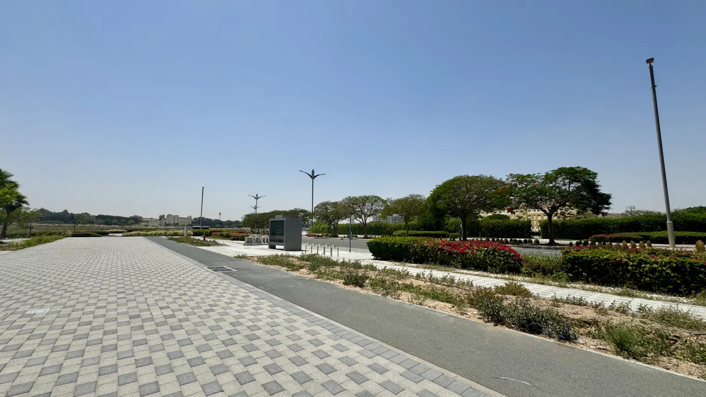 Outdoor view of a paved walkway, bike rack, and green trees under a clear blue sky.
