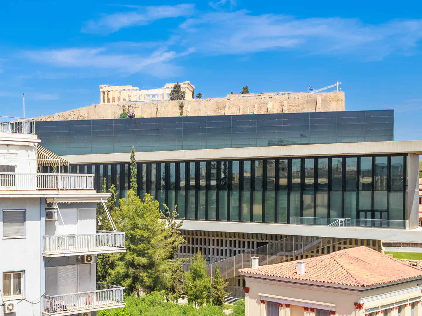 View of the Acropolis Museum in Athens, Greece, with the Acropolis visible in the background under a blue sky.