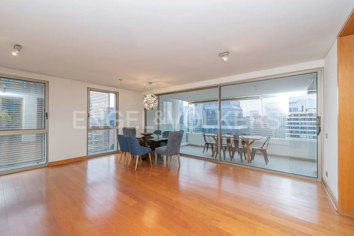 Modern dining room with hardwood floors, blue chairs, a glass table, and a balcony overlooking a city skyline.