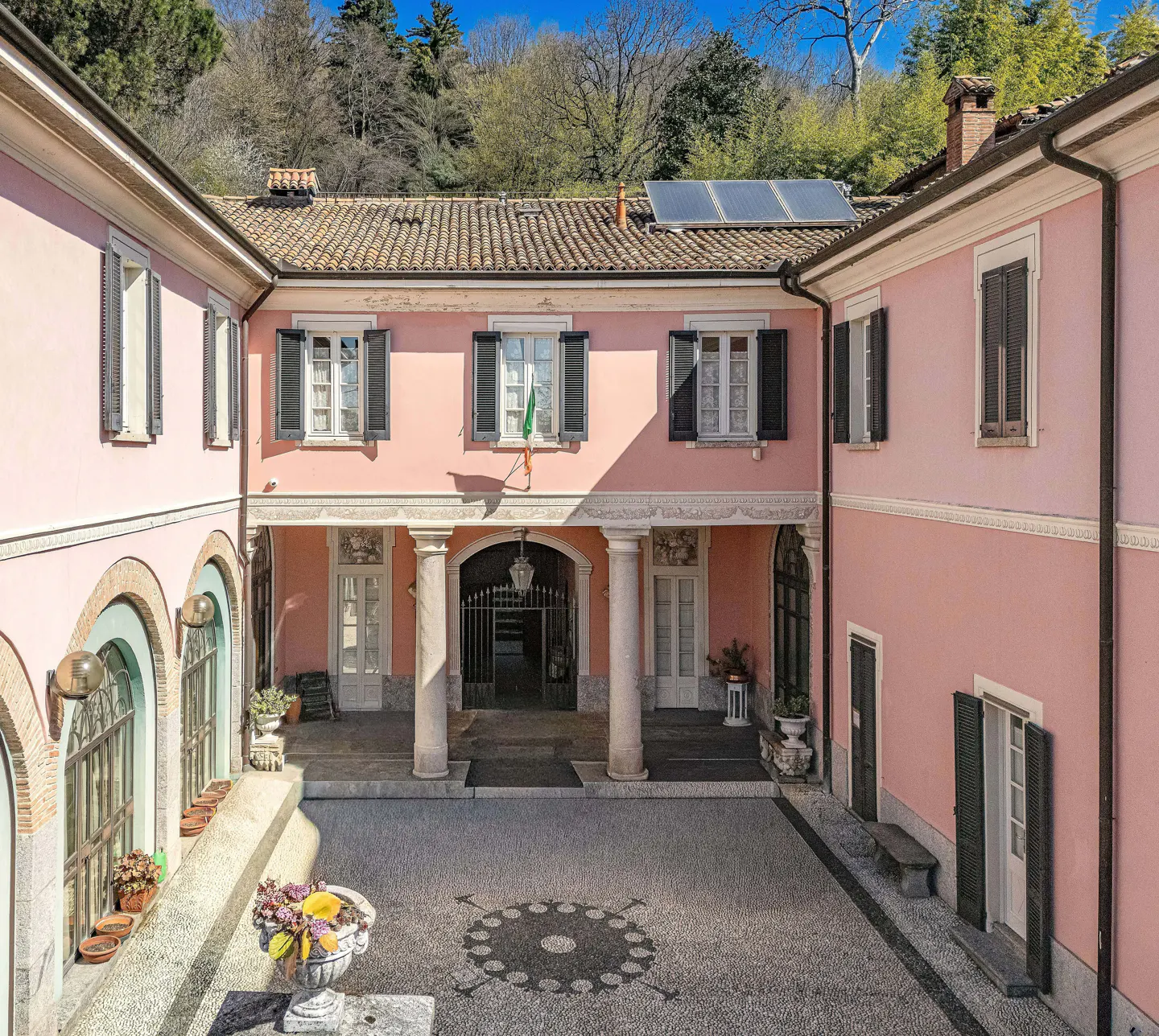Exterior view of a pink villa with black shutters, a courtyard, and a tiled roof with solar panels.