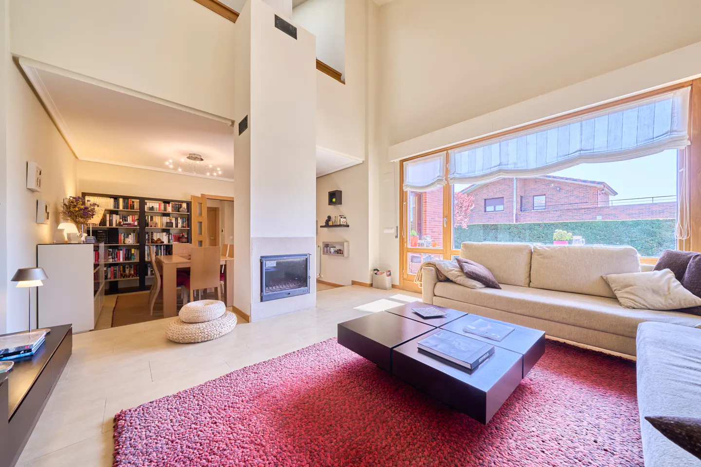 Bright living room with a red rug, a beige sofa, and a black coffee table. A fireplace and a bookcase are also visible.