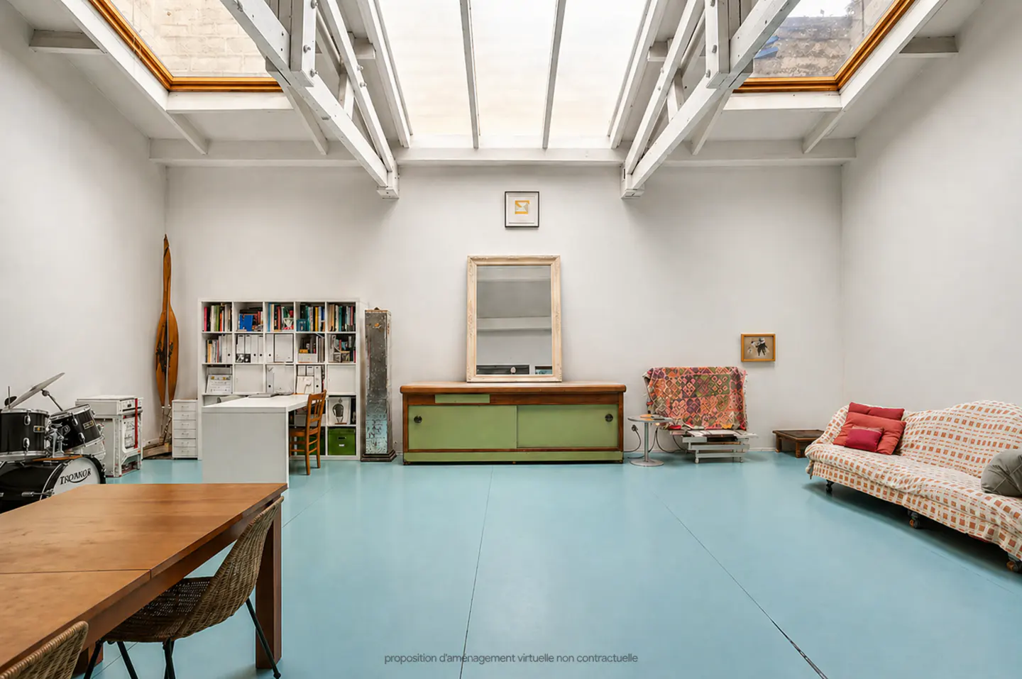 Bright, airy room with white walls, blue floor, and skylights. Features a table, sofa, desk, bookshelf, and drum set.