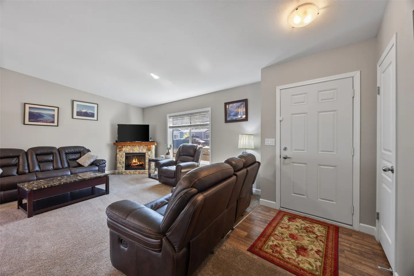 Living room with brown leather sofas, stone fireplace with TV, and white front door with floral rug.