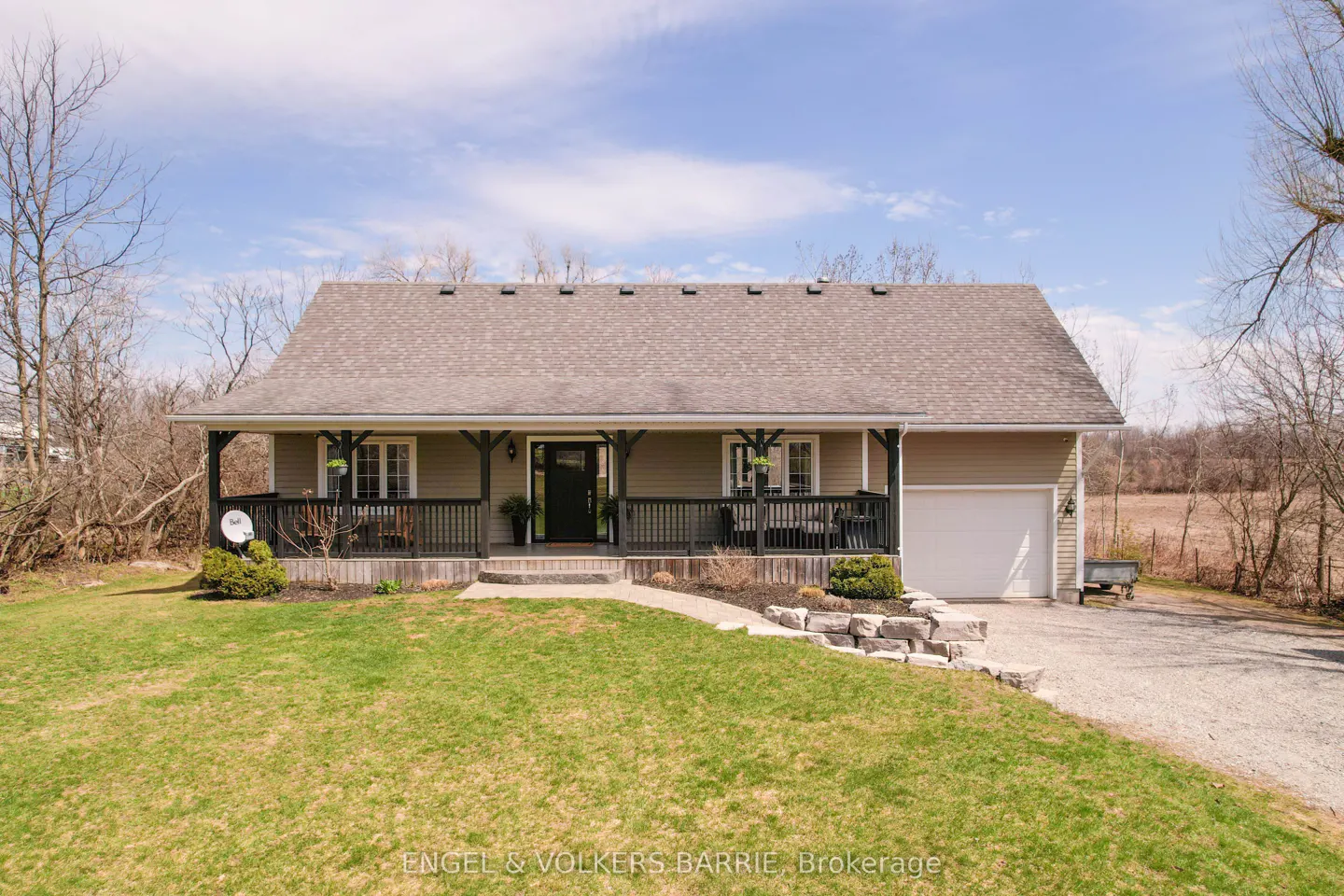 Tan house with a covered porch and black railings, a gray roof, and a green lawn on a sunny day.