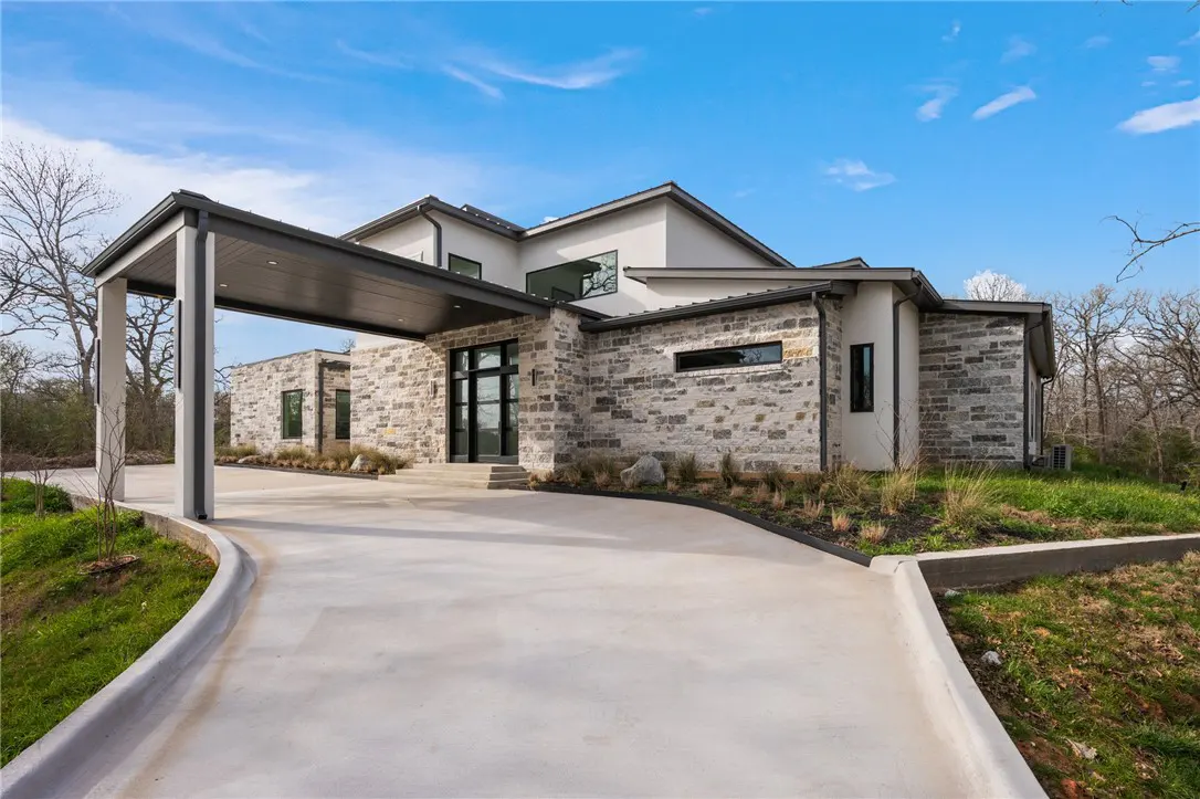 Modern stone house with a covered driveway. The house has a black front door and black framed windows. Blue sky in the background.