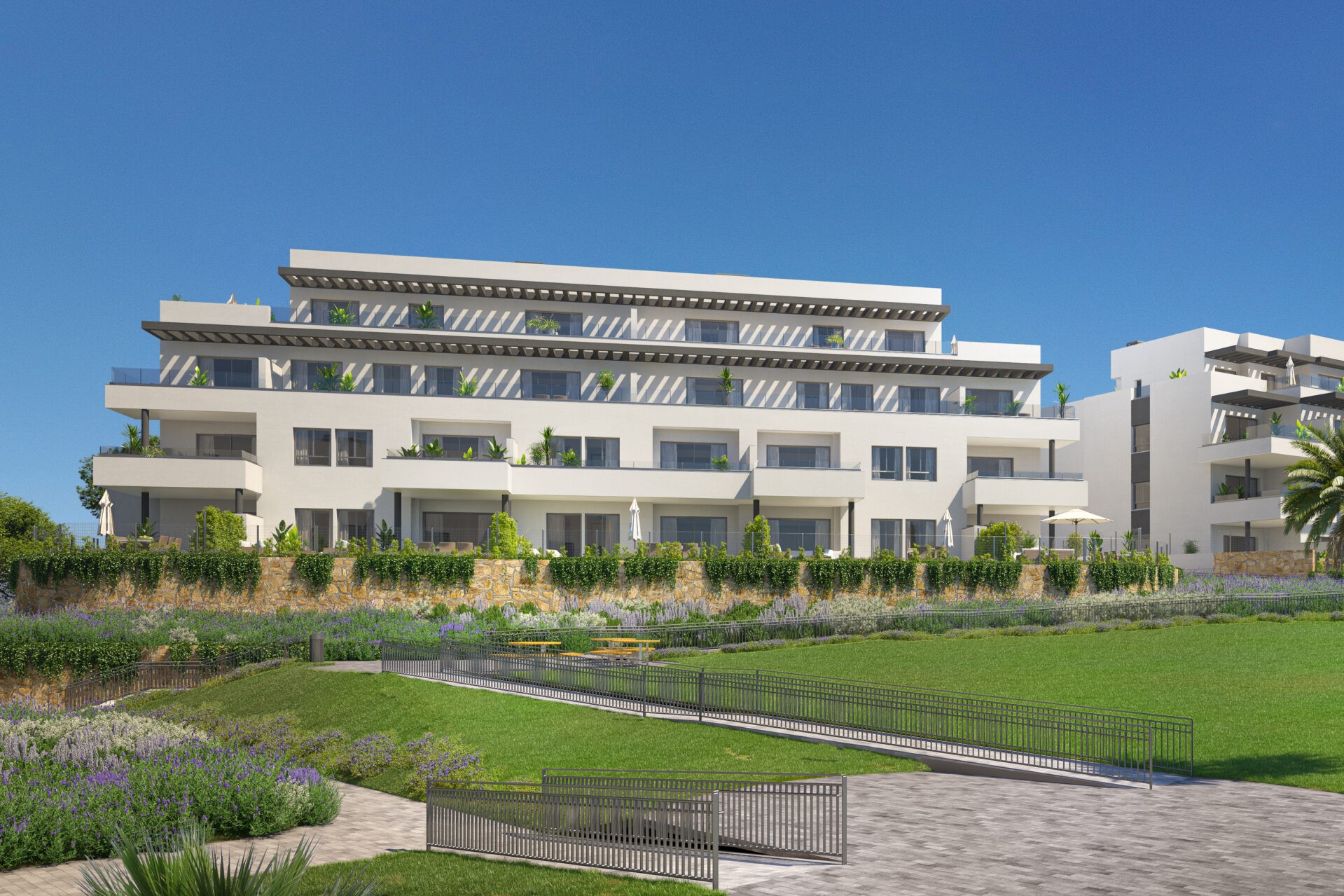 Modern white apartment building with balconies and a landscaped lawn under a clear blue sky.