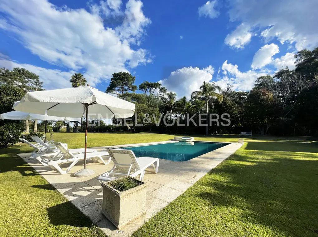 A backyard with a pool, lounge chairs, and a white umbrella on a sunny day. The Engel & Volkers logo is visible.