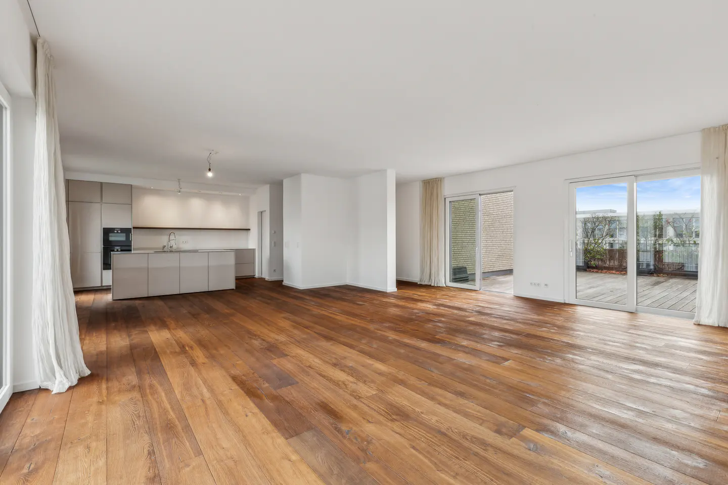 Bright, open-concept apartment with hardwood floors, white walls, and a modern kitchen. Sliding glass doors lead to a balcony.