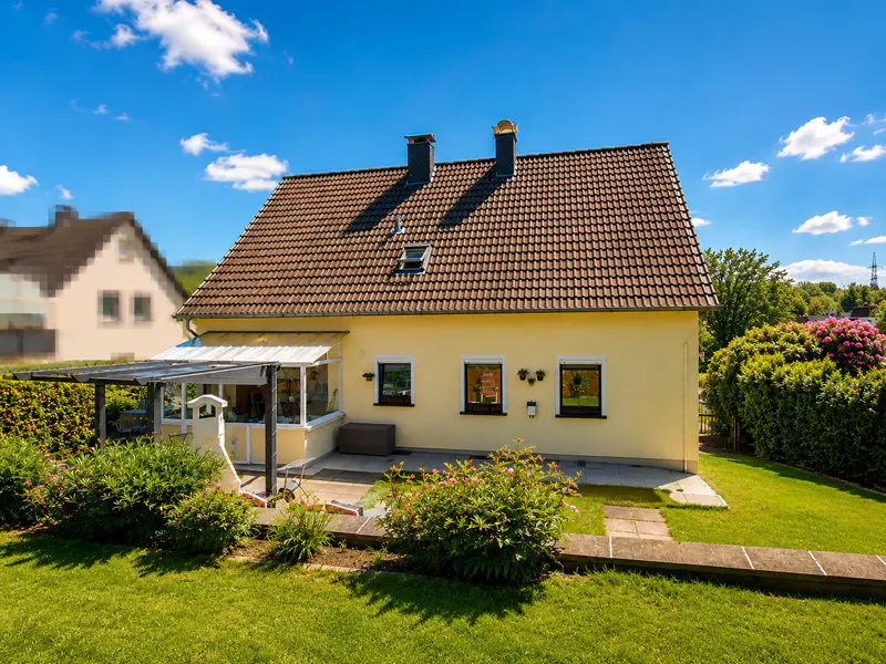 Back view of a yellow two-story house with a brown tiled roof, a glass-enclosed patio, and a lush green lawn.