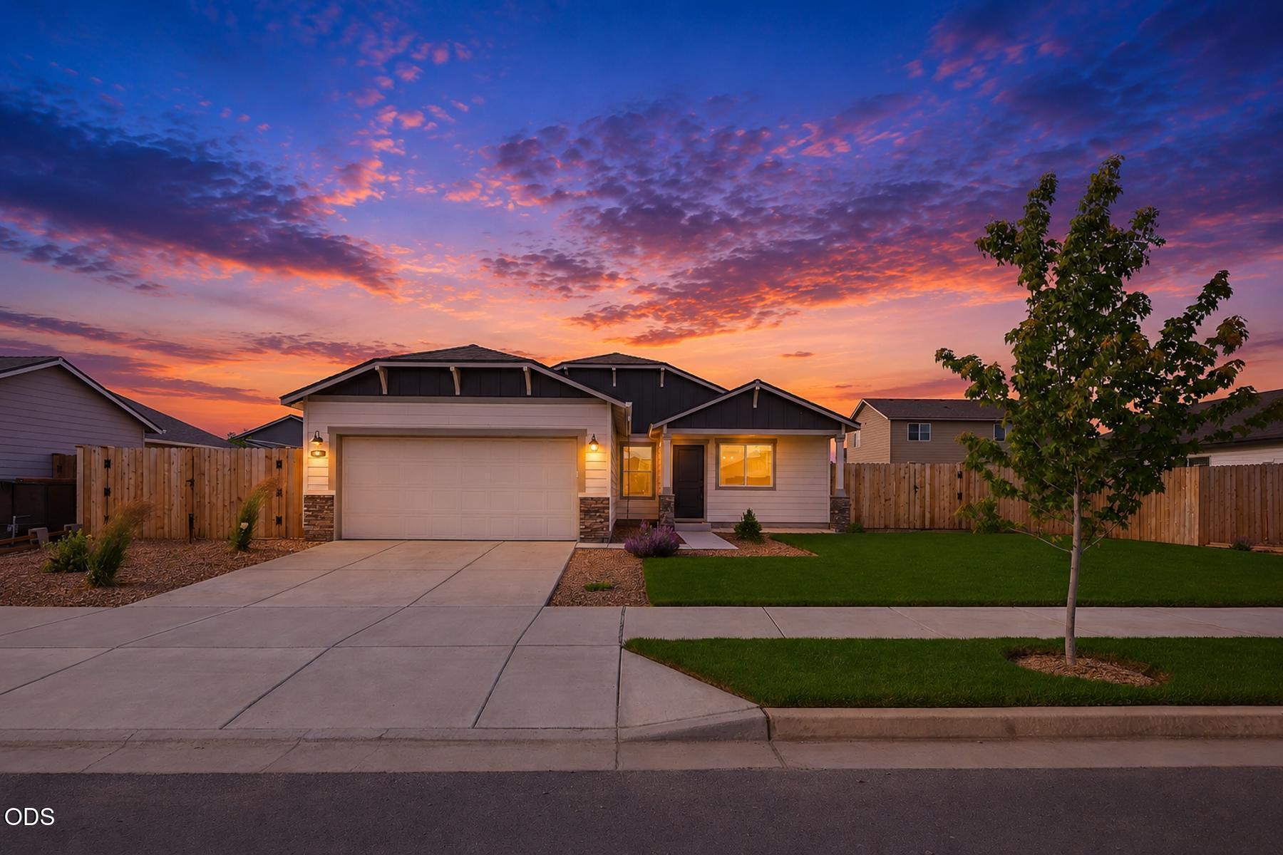 Single-story suburban home with a two-car garage and green lawn under a vibrant purple and orange sunset sky.