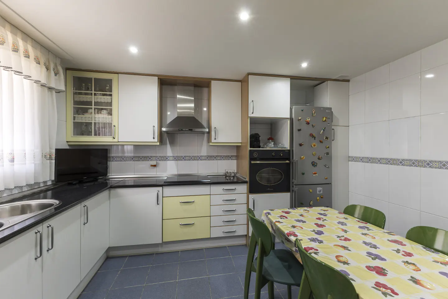 A kitchen with white cabinets, black countertops, and a table with green chairs.