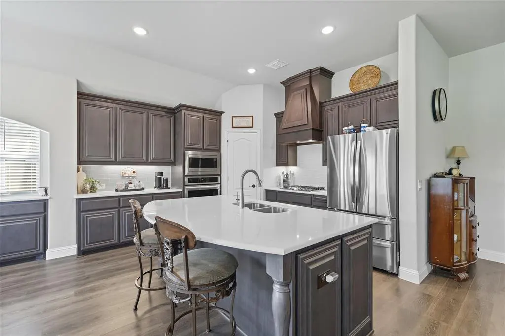 A modern kitchen with dark wood cabinets, stainless steel appliances, and a white countertop island with two stools.