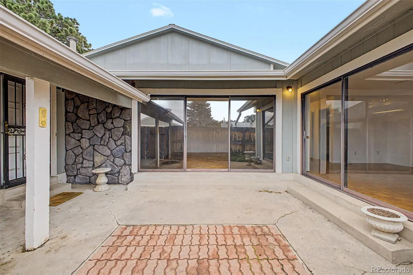 Exterior view of a light blue house with a stone wall, sliding glass doors, and a brick patio.