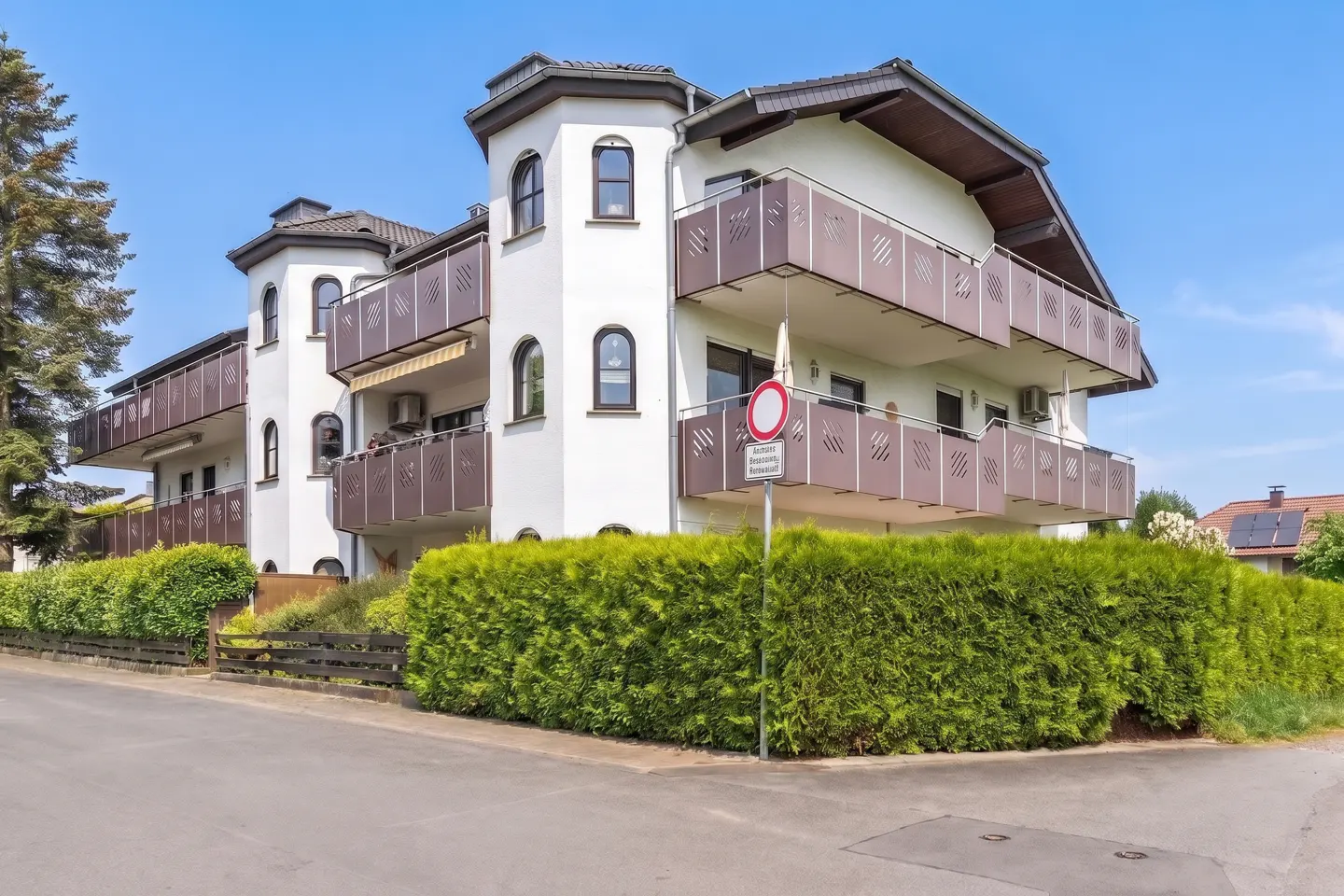 A three-story white building with brown balconies and a turret on a sunny day.