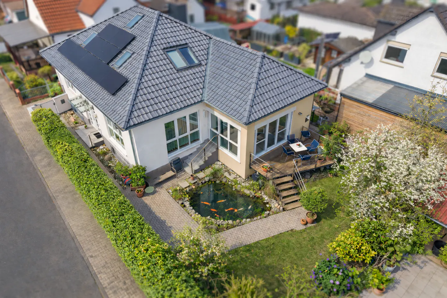 Aerial view of a house with solar panels, a pond with koi fish, and a deck with outdoor furniture.