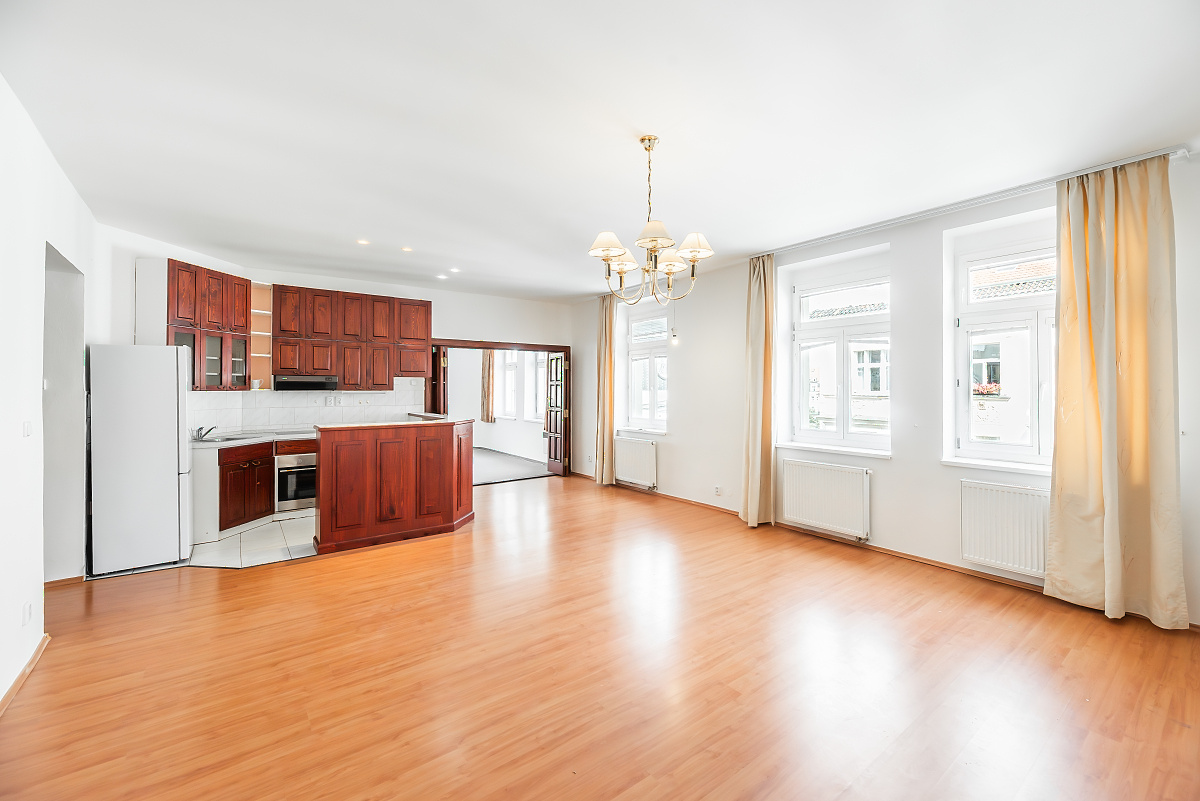 Spacious open-plan room with wood floors, a wooden kitchen island, white walls, and a classic chandelier. [AI-generated text]