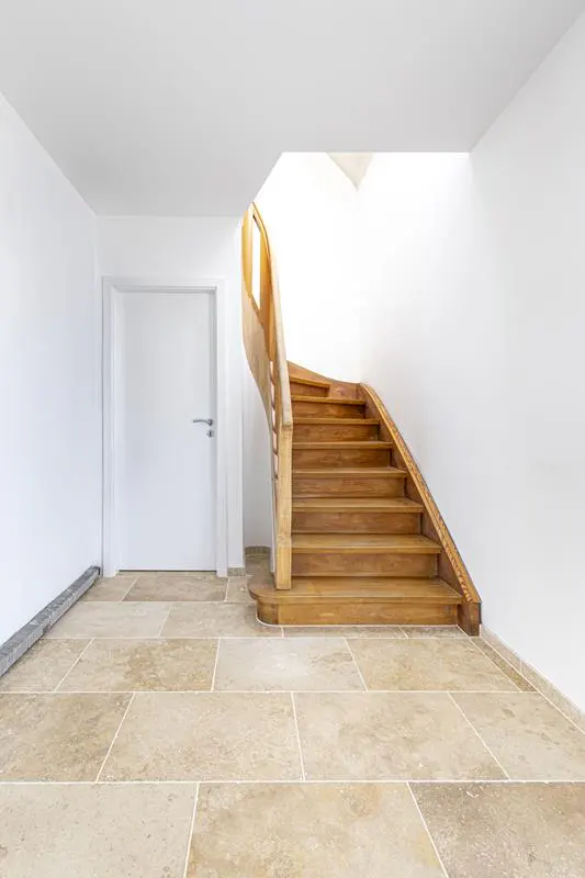 A bright entryway with light stone tile flooring, a white door, and a wooden staircase leading to an upper level.