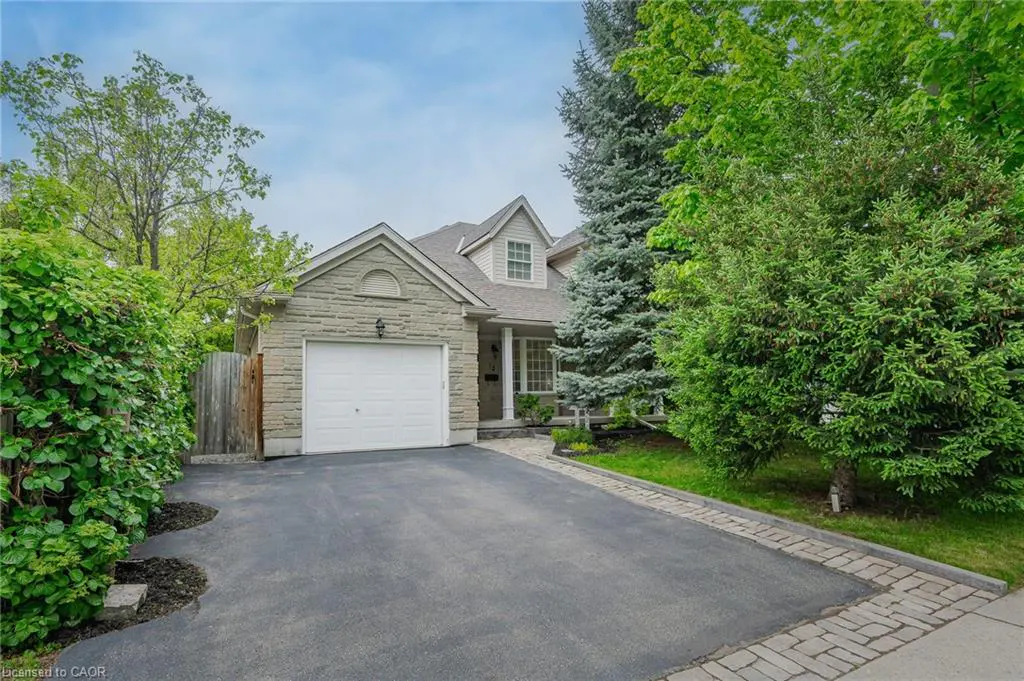 A single-family home with a stone facade and a white garage door, surrounded by green trees and a black asphalt driveway.