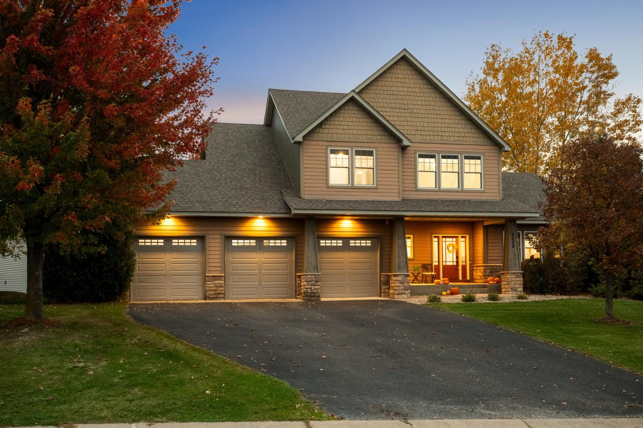 Two-story suburban home with a three-car garage, stone accents, and autumn trees at dusk with warm exterior lighting. [AI-generated text]