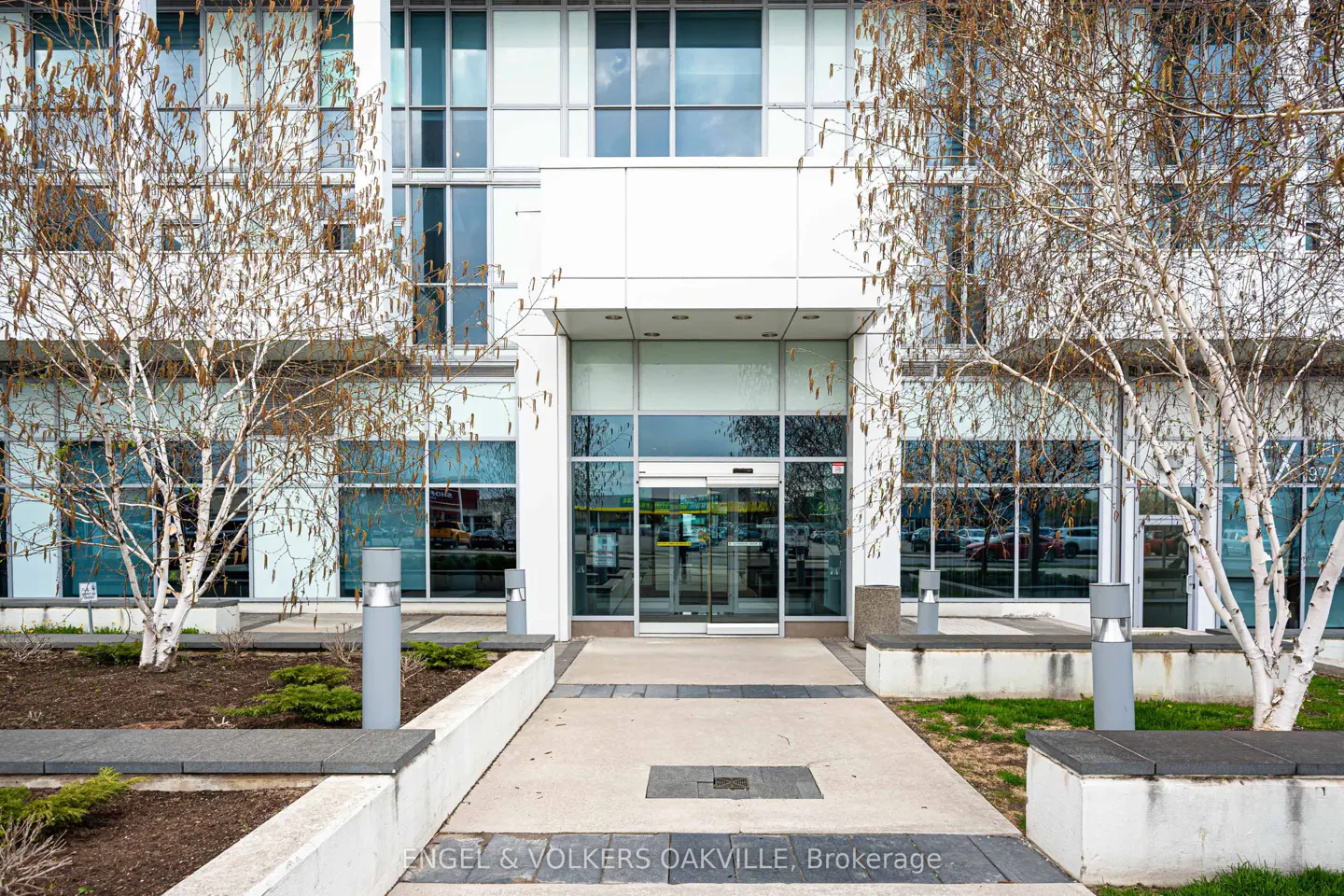 Exterior of a modern white building with glass windows and automatic doors. Trees flank the entrance.