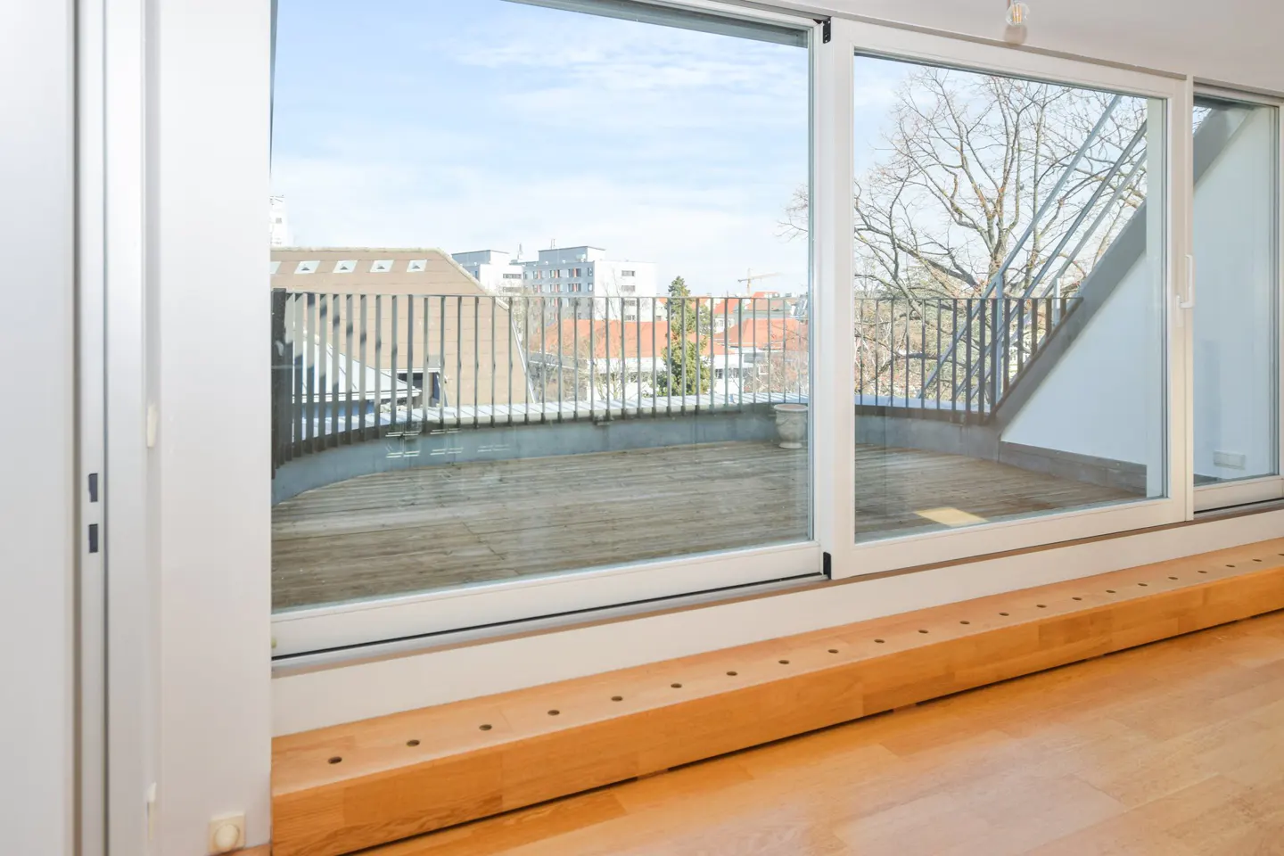Bright room with a large sliding glass door leading to a balcony with a view of city buildings.