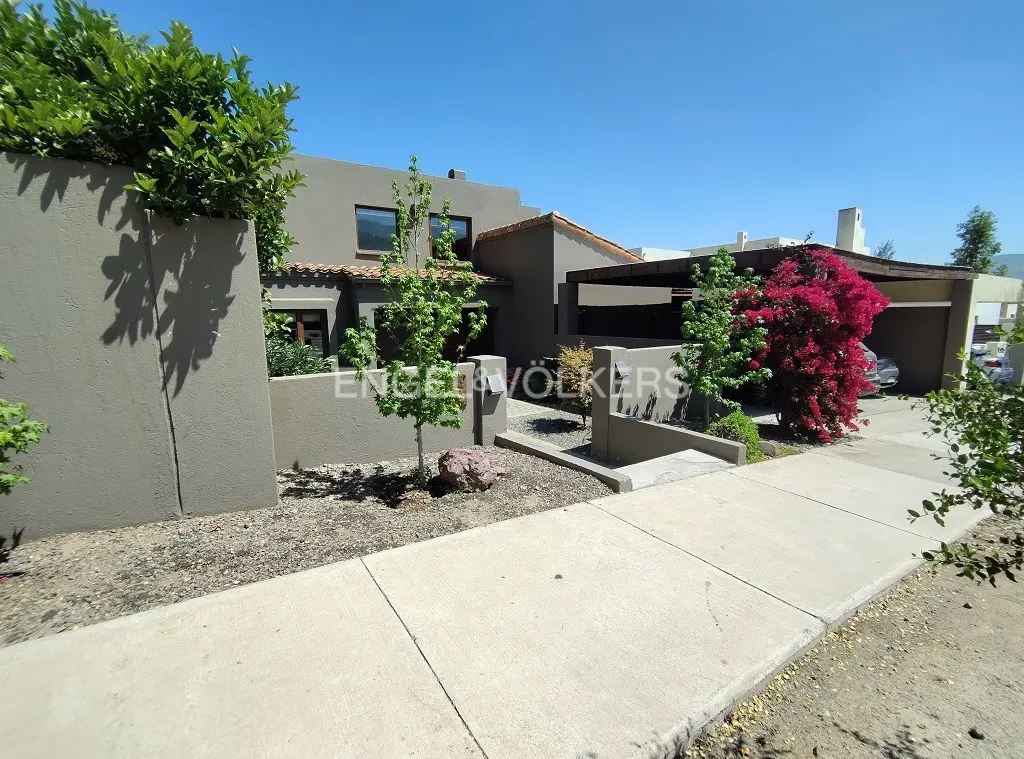 Exterior view of a modern, two-story house with a carport, gray walls, and lush green landscaping.