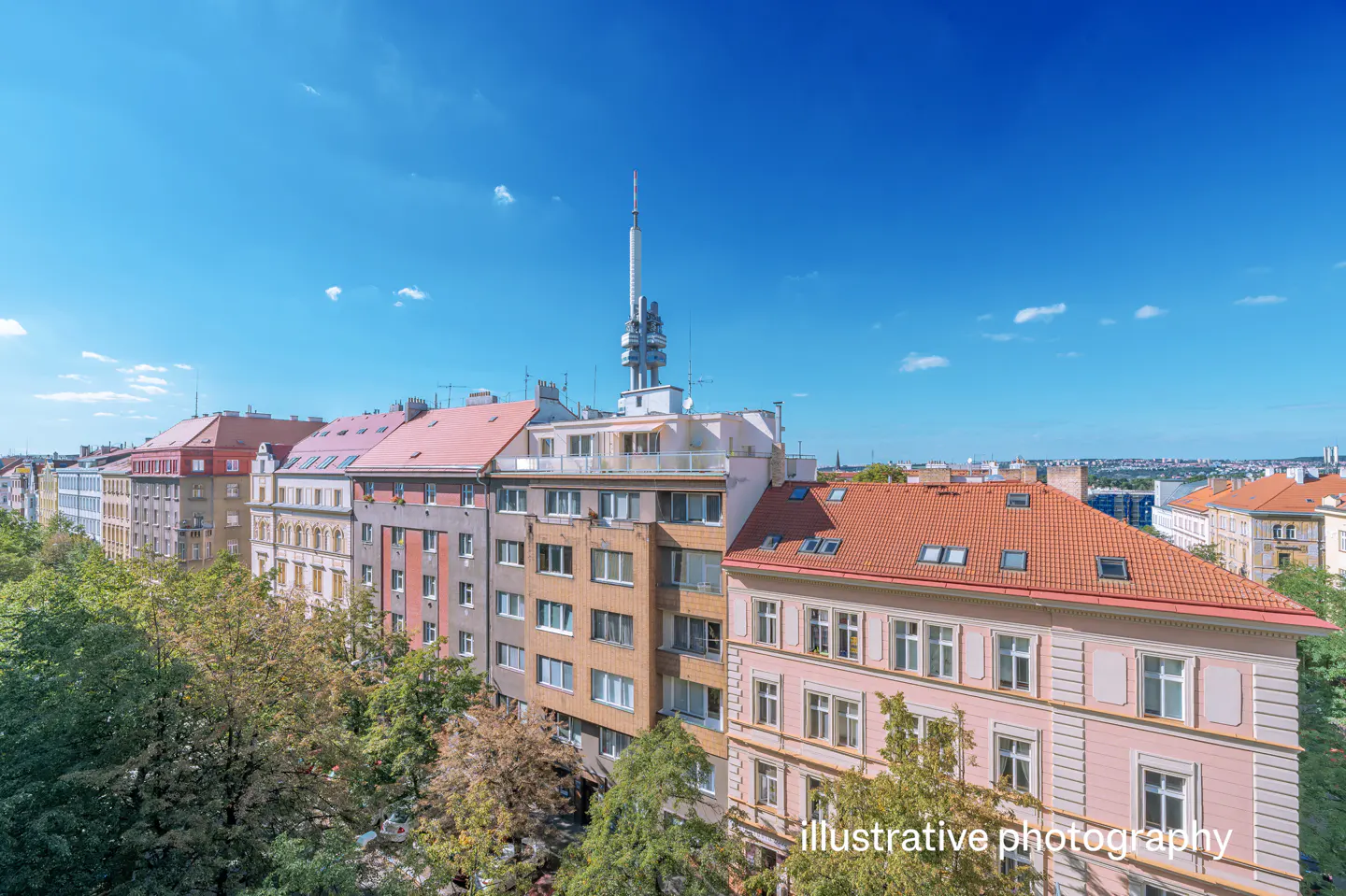 Cityscape view of Prague with colorful buildings, trees, and the Žižkov Television Tower under a blue sky.