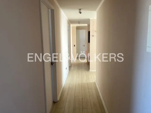 A bright hallway with light wood floors and pale pink walls leads to a white door. The Engel & Völkers logo is visible.