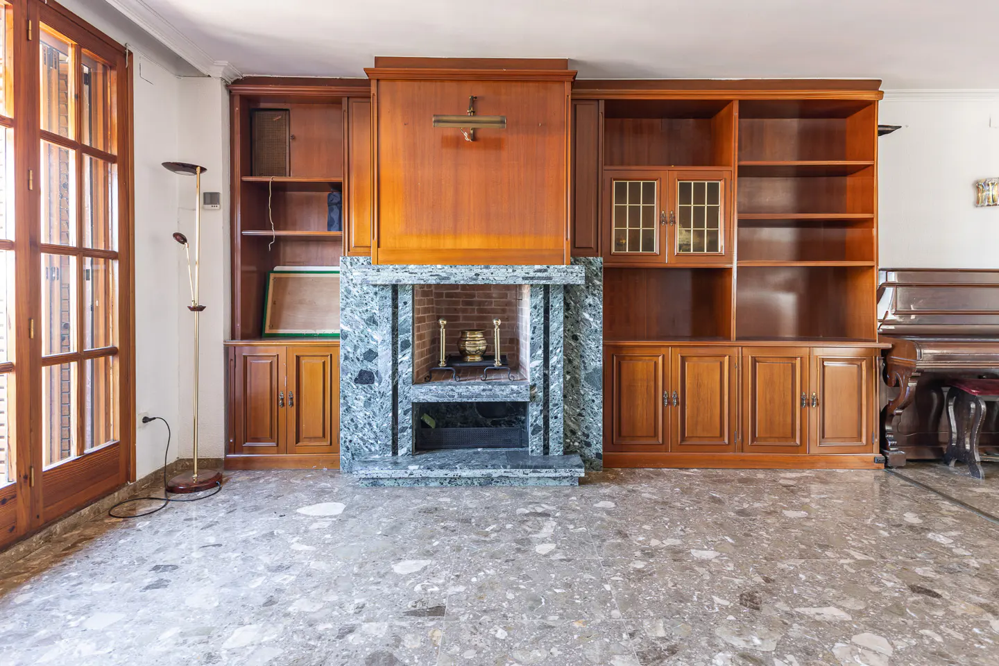 Living room with a marble fireplace, wooden built-in shelves, a piano, and a gray terrazzo floor.