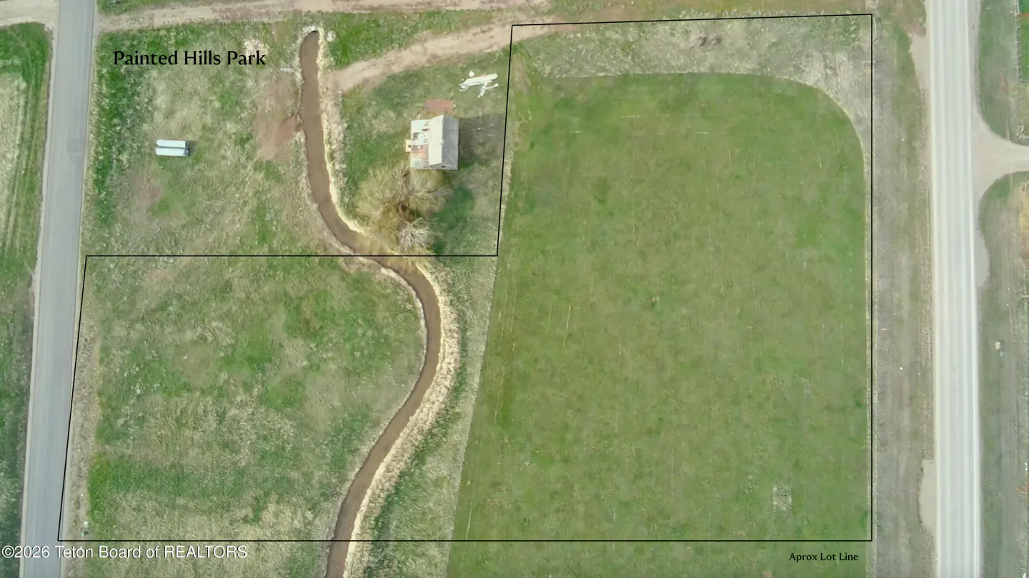 Aerial view of a green field with a winding stream, a small building, and a road on the right.