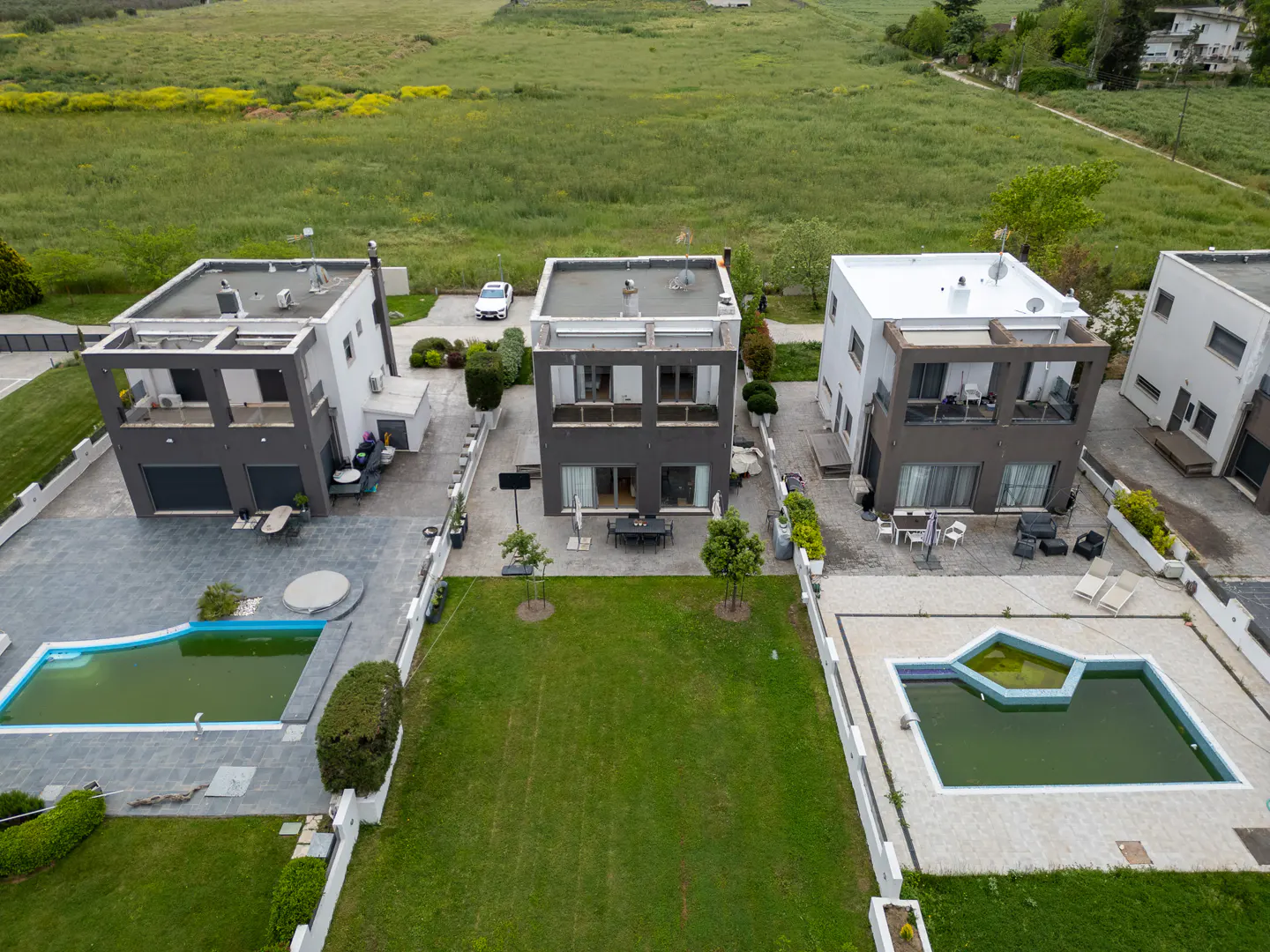 Aerial view of modern two-story homes with pools and green lawns on a cloudy day.