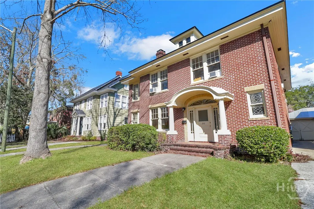Brick two-story house with white door and trim, green lawn, and sidewalk on a sunny day.