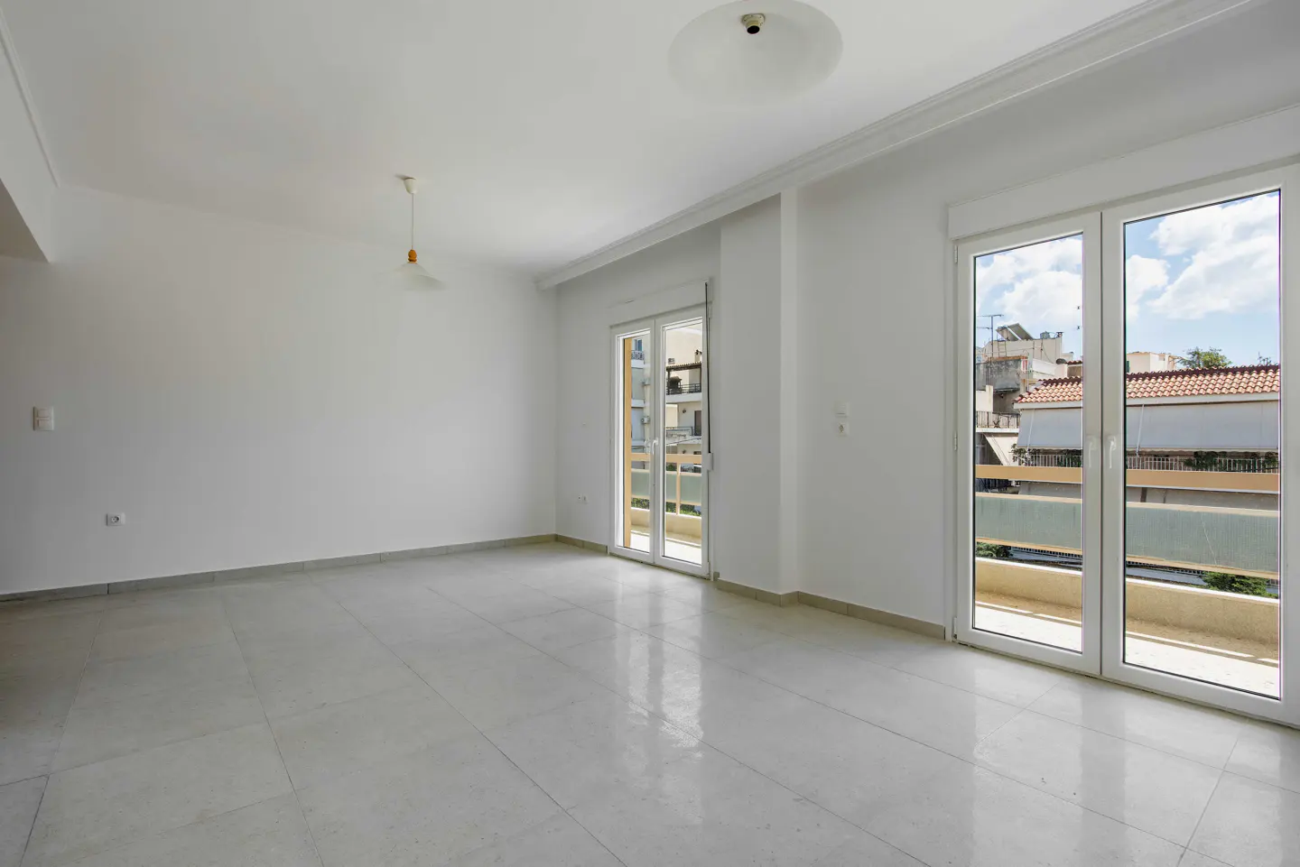 Bright, empty room with white walls, tile floor, and two sets of glass doors leading to balconies.
